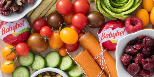 Babybel cheese on a counter with vegetables, nuts and dried fruit