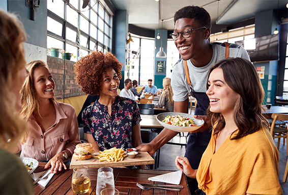 Smiling server bringing two plates of food to a table in a restaurant