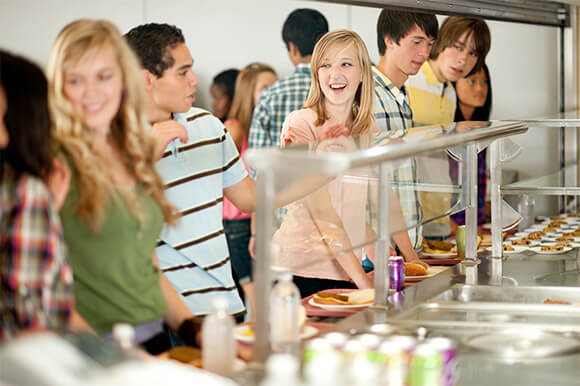 Lauging teenagers grabbing food in a cafeteria line