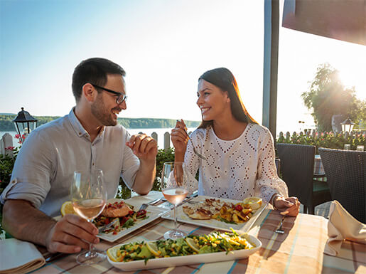 A couple smiling and laughing while enjoying delicious food at an outdoor table at a restaurant