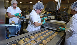 Workers wearing hairnets and gloves working on a Kaukauna assembly line