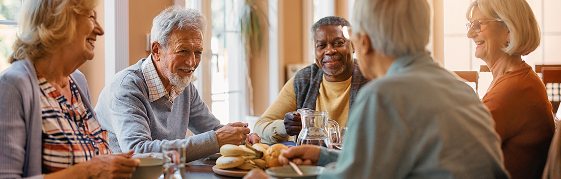 Group of elderly people smiling and laughing over coffee, fruit and muffins