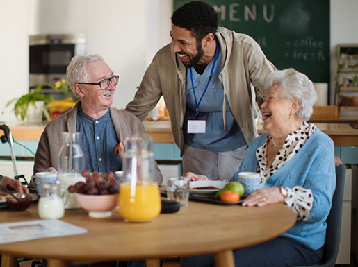 Healthcare worker laughing with an elderly man and woman who are enjoying breakfast